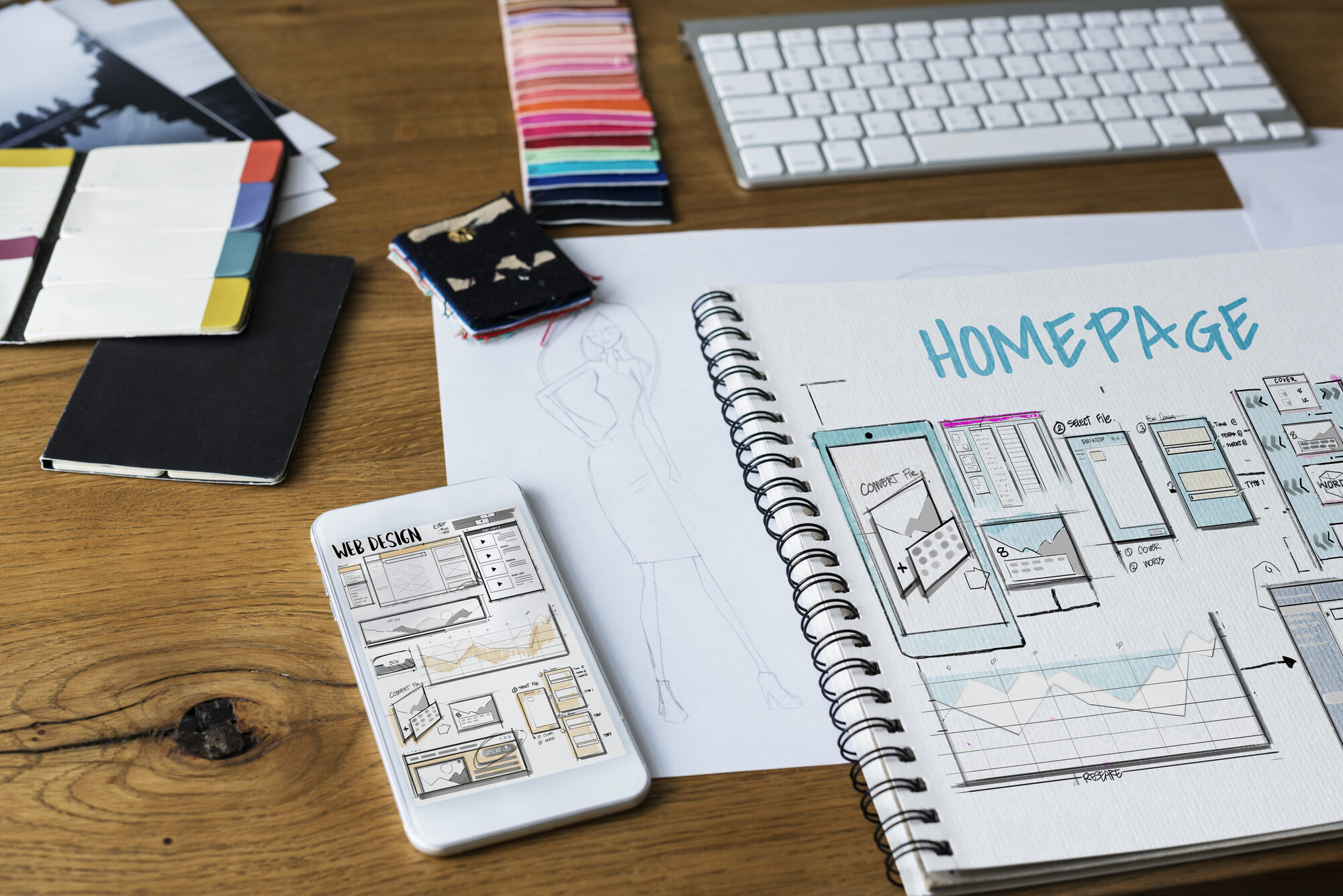 Handskizze eines Homepage-Layouts im Notizbuch neben Tastatur und Farbmustern